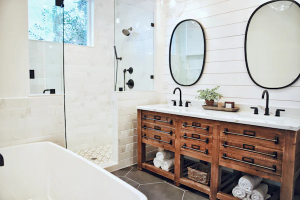 Bathroom with a wood double vanity, round mirrors, white tile, and a soaking tub