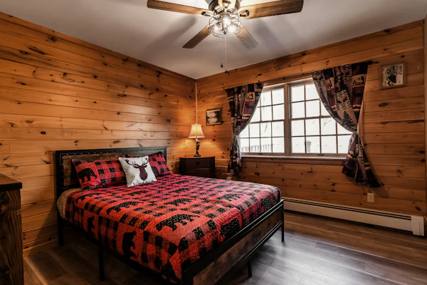 Pine-paneled bedroom with a king bed in red plaid and a ceiling fan